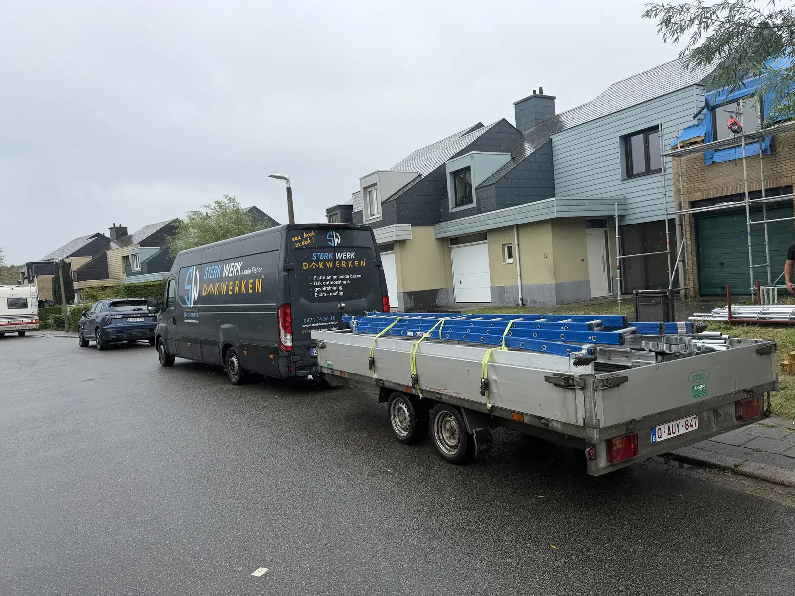 Bestelwagen met aanhangwagen vol stellingmateriaal voor een afgewerkte woning met leien dak