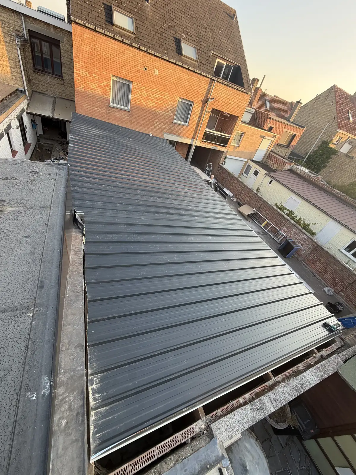 Dak met staande naad in donker zink op een aanbouw, gefotografeerd bij avondlicht
